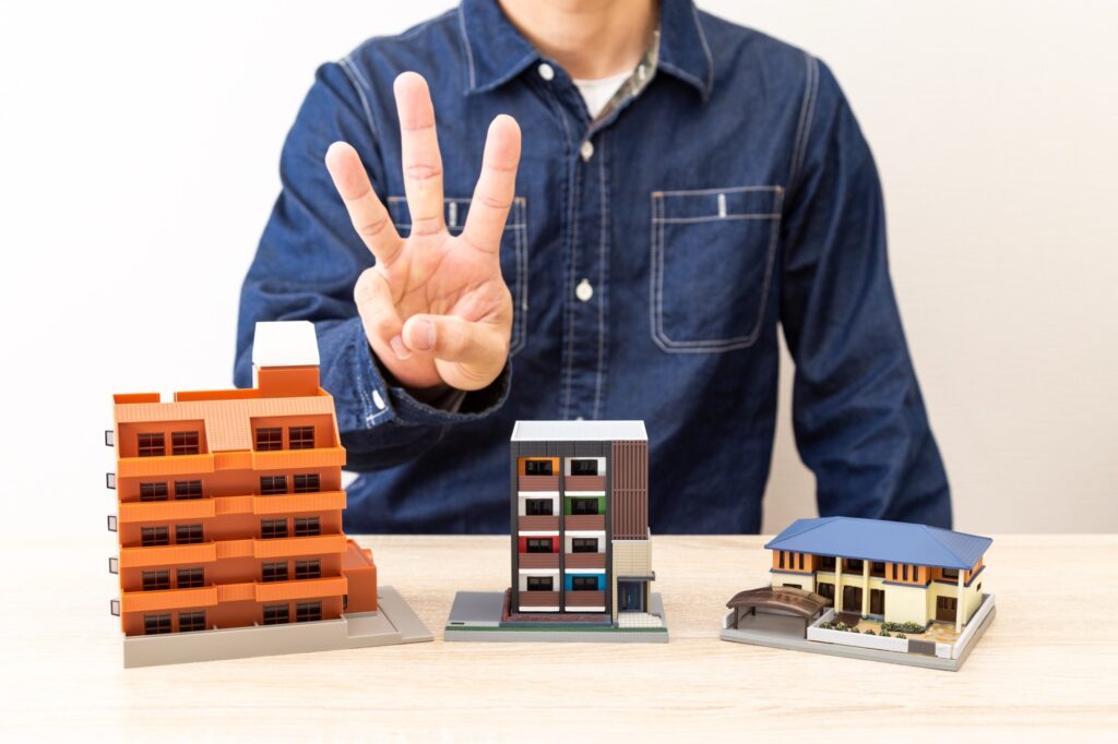 住宅模型の前で3を示す男性